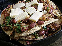 Layering Chapati pieces, Tomato, chutney, red beans and cheese in an iron skillet